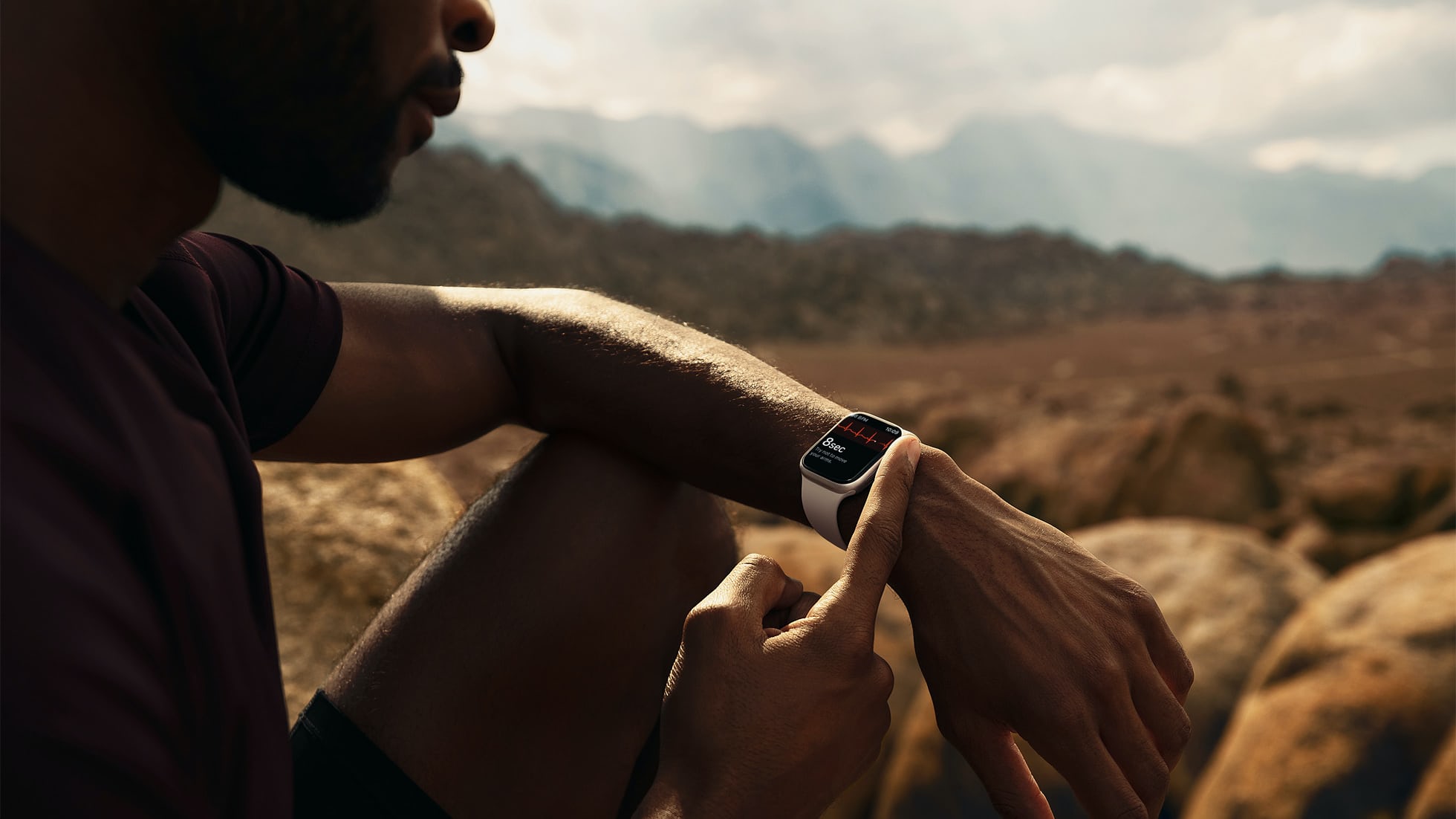 一名男子坐在沙漠中檢查他的 Apple Watch。