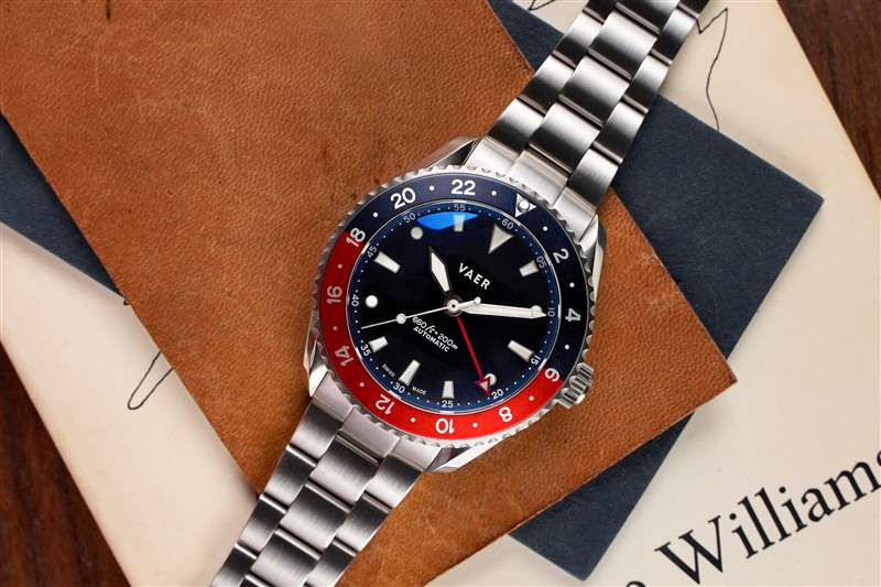 一塊帶有紅色和藍色表圈的 GMT 手表放在一塊棕色皮革上。